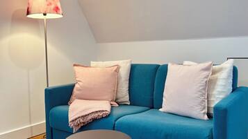 Ein modernes Wohnzimmer mit einem blauen Sofa, einem kleinen runden Tisch, einer Stehlampe und einem gemusterten Teppich.
