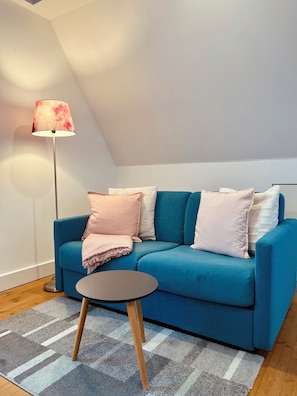 Una sala de estar moderna con un sofá azul, una mesita redonda pequeña, una lámpara de pie y una alfombra estampada.