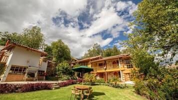 Una casa de dos pisos con un patio, una mesa de comedor con sillas y un paraguas verde.