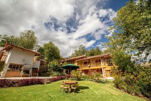 A two-story house with a patio, a dining table with chairs, and a green umbrella. - Iorana hotel Urubamba (Urubamba)