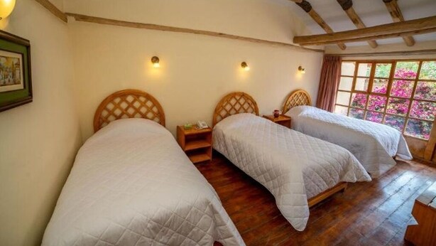 A room with three beds, wooden beams on the ceiling, and a window with pink flowers. - Iorana hotel Urubamba (Urubamba)