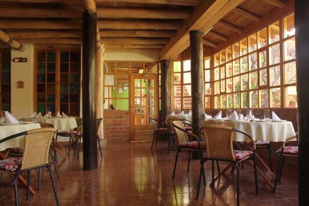 A restaurant with wooden beams, tiled floors, and large windows. Tables are set with white tablecloths and chairs.