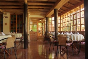 A restaurant with wooden beams, tiled floors, and large windows. Tables are set with white tablecloths and chairs. - Iorana hotel Urubamba (Urubamba)
