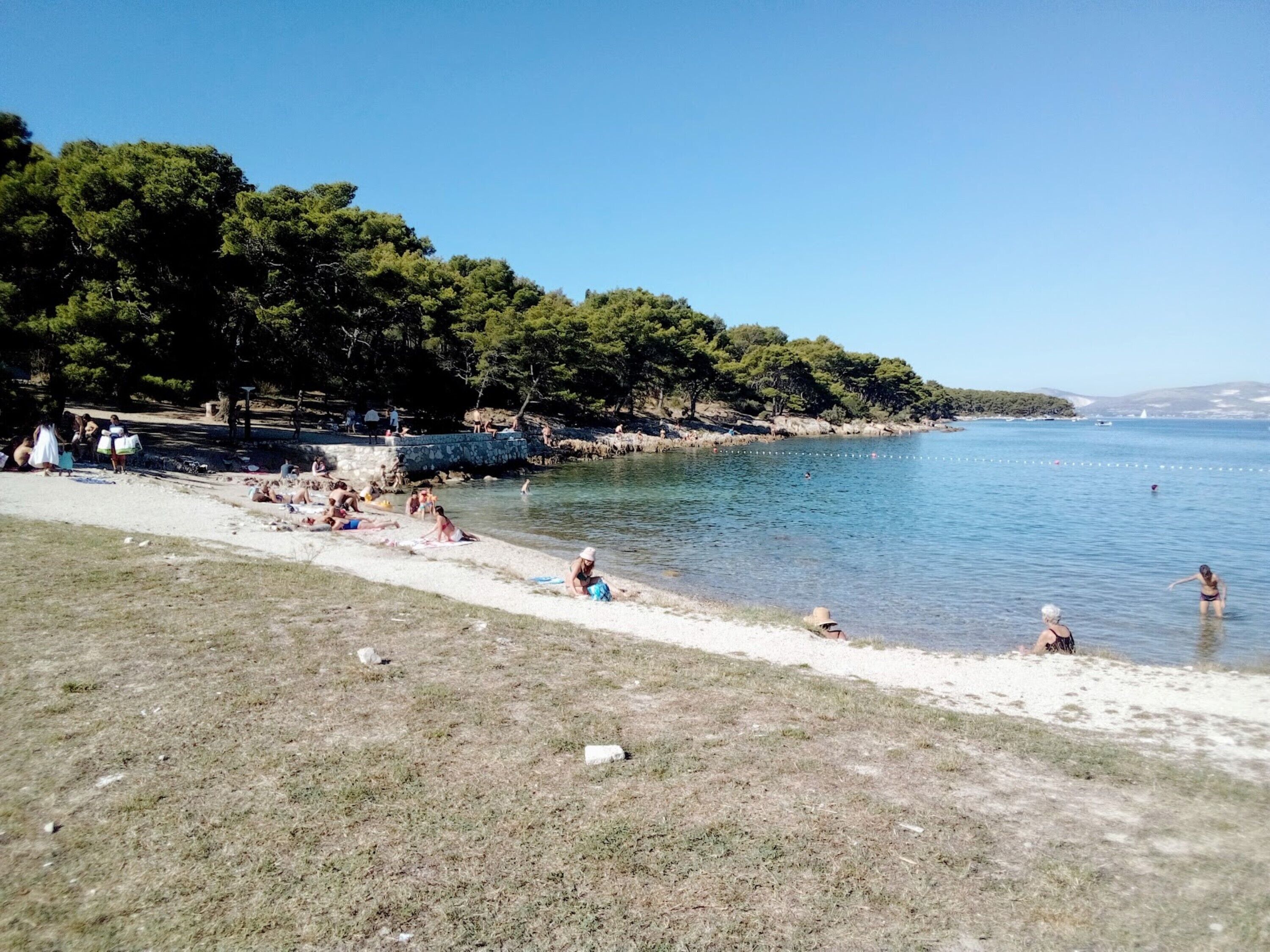 Une plage où des gens se prélassent au soleil et se baignent, entourée d’arbres et sous un ciel dégagé.