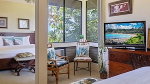 A bedroom with a bed, a television, and a window with a view of a beach. - Grand Champions Villas in Wailea, Maui (Kihei)