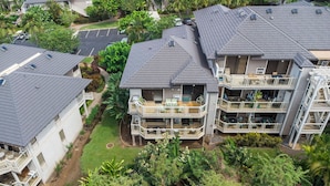 A multi-story residential building with a balcony on the second floor, a covered outdoor seating area, and a parking lot in the background. - Grand Champions Villas in Wailea, Maui (Kihei)