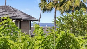A wooden structure with a tiled roof, surrounded by lush greenery and palm trees, overlooking a body of water. - Grand Champions Villas in Wailea, Maui (Kihei)
