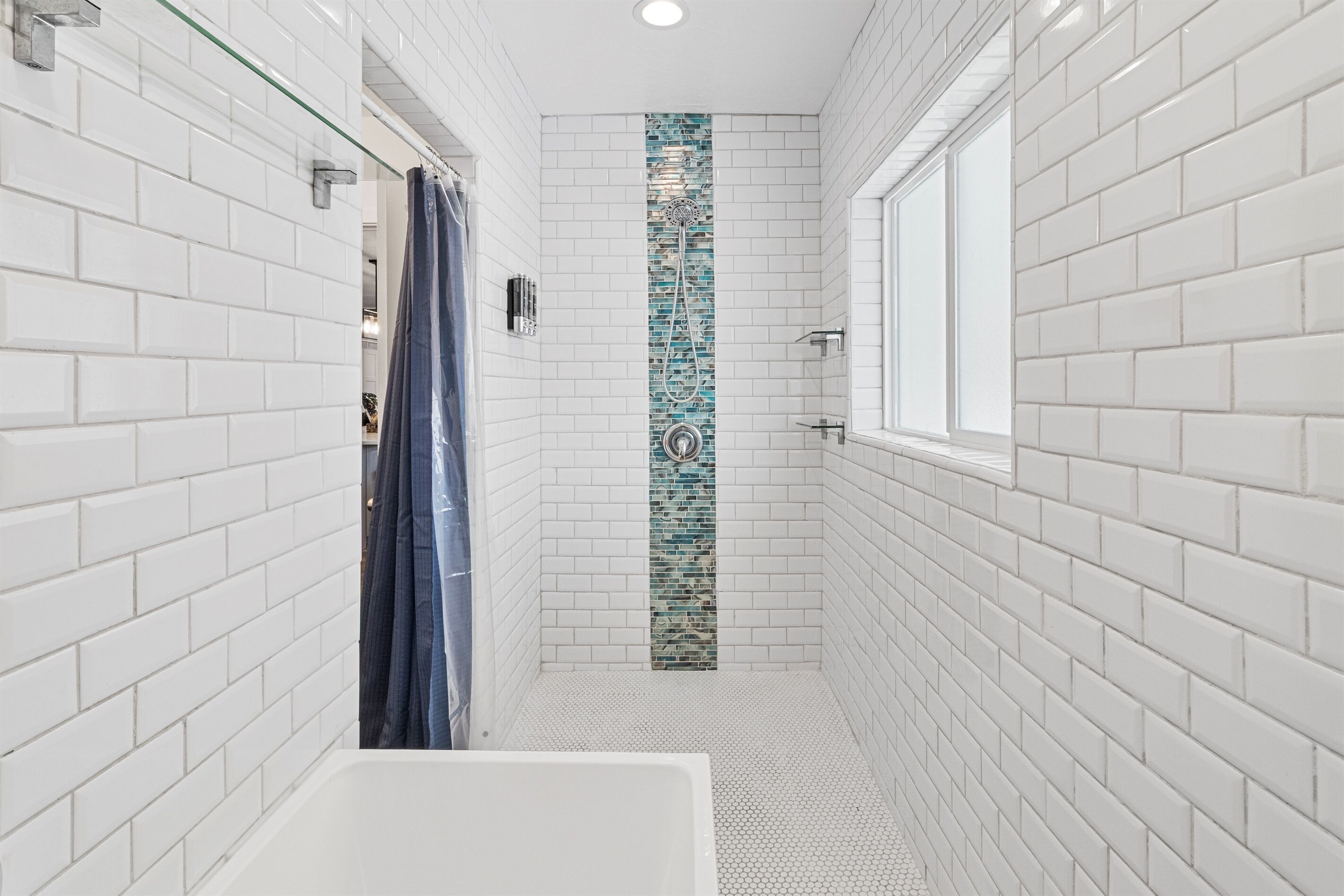 A modern bathroom with white subway tiles, a glass shower enclosure, and a window providing natural light.
