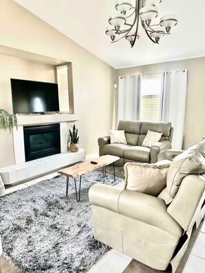 A living room with a fireplace, a sofa, a TV, and a chandelier.