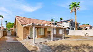 Un immobile residenziale con patio coperto, garage e giardino curato con palme.