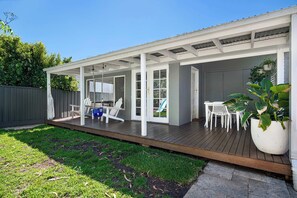 A covered patio area with a wooden deck, white furniture, and a large potted plant. - Family Home - Books, Yard & Central Location (Mayfield East)