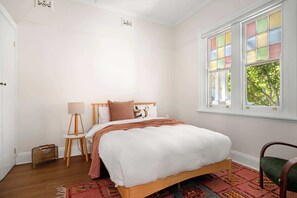 A bedroom with a wooden bed, a window with colorful panes, a standing lamp, and a patterned rug. - Family Home - Books, Yard & Central Location (Mayfield East)