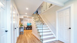Un intérieur moderne avec un escalier en bois, des portes blanches et un coin repas agrémenté d’un lustre.