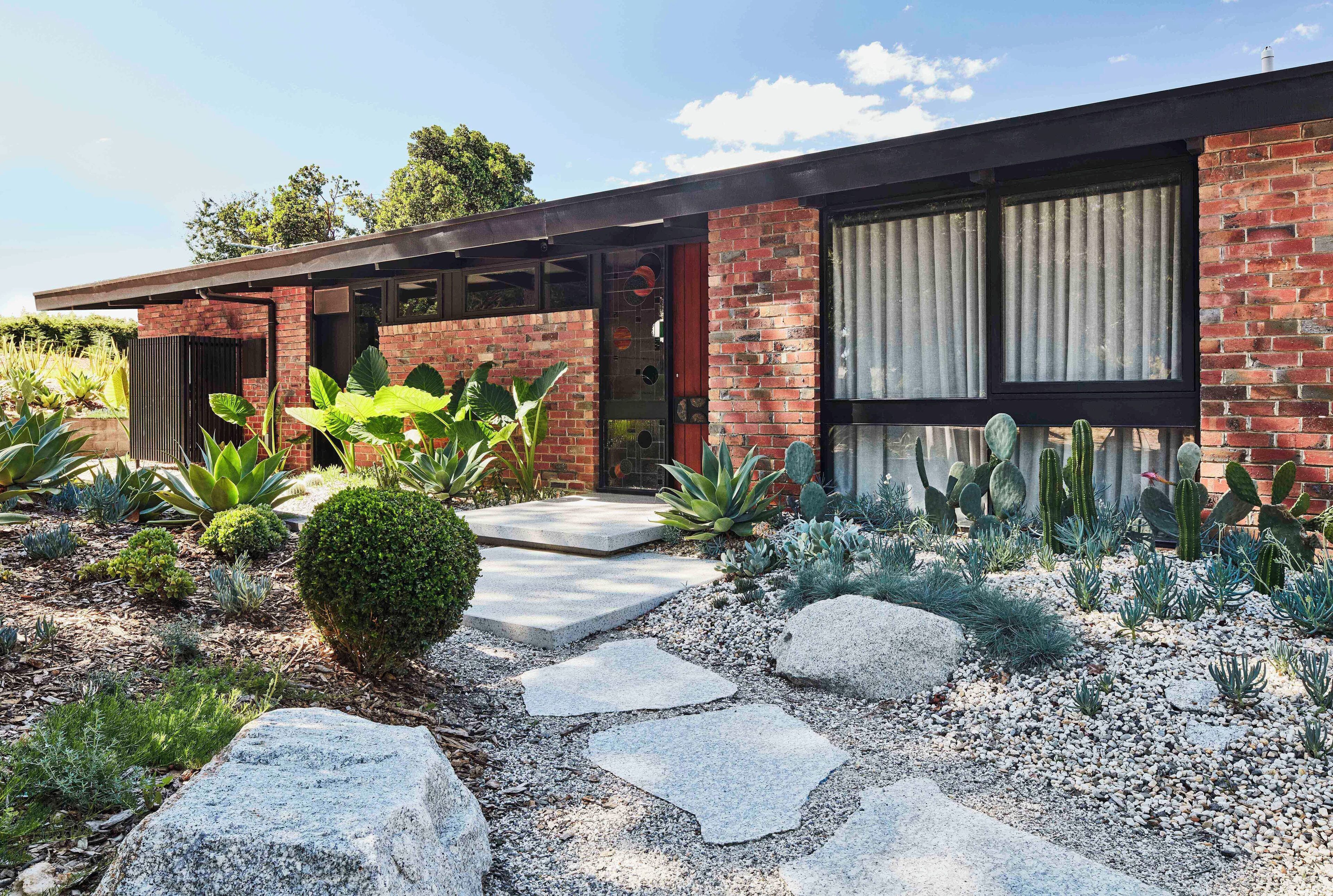 A modern house with a brick exterior, large windows, and a well-maintained garden with various plants and a stone pathway.