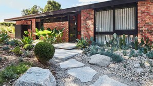 Una casa moderna con fachada de ladrillo, ventanas amplias y un jardín bien cuidado con diversas plantas y un sendero de piedra.