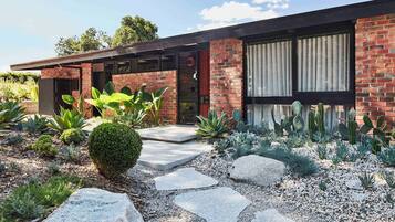 A modern house with a brick exterior, large windows, and a well-maintained garden with various plants and a stone pathway.