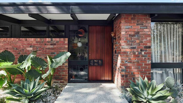 Una casa moderna con fachada de ladrillo, puerta de madera y ventanas grandes.