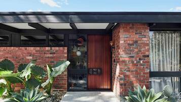 A modern house with a brick facade, a wooden door, and large windows.