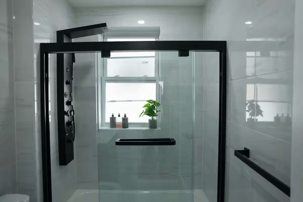 A modern bathroom with a glass shower enclosure, a white toilet, and a window with a plant.