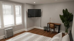 A bedroom with a bed, a desk, a chair, a potted plant, and a television. - Bright & Modern 3-Bed House ~ Parking Included ~ Near Transit in East Flatbush (Brook)