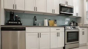 A modern kitchen with white cabinets, a stainless steel dishwasher, a microwave, and an oven. - Bright & Modern 3-Bed House ~ Parking Included ~ Near Transit in East Flatbush (Brook)