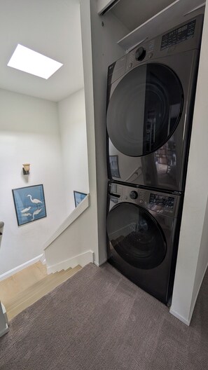 A laundry room with two stacked washers and dryers, a staircase with a light fixture, and a framed picture on the wall. - Sausalito Retreat with Water Views and AC -- 30-DAY MINIMUM STAY JUNE 26 - AUG 8 (Sausalito)
