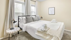 A neatly arranged bedroom with a bed, pillows, a bedside table with a lamp, and a framed artwork on the wall. - Modern 2BDR Condo in Ohio City (Cleveland)