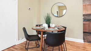 A dining area with a round table set for four, surrounded by black chairs. A potted plant is on the table, and a mirror hangs on the wall. - Modern 2BDR Condo in Ohio City (Cleveland)