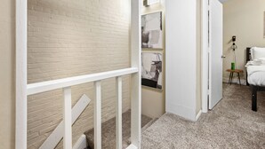 A hallway with a white railing, a brick wall, and a carpeted floor. - Modern 2BDR Condo in Ohio City (Cleveland)