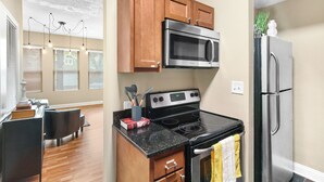 A modern kitchen with wooden cabinets, a stainless steel microwave, a black stove, and a refrigerator. - Modern 2BDR Condo in Ohio City (Cleveland)