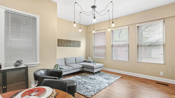A modern living room with a sectional sofa, a dining table set for two, and a chandelier. - Modern 2BDR Condo in Ohio City (Cleveland)