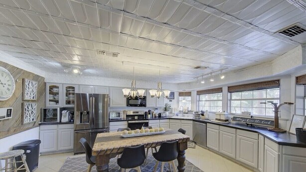 A modern kitchen with white cabinetry, stainless steel appliances, a wooden dining table, and pendant lighting. - Paradise Canyon (Ingram)
