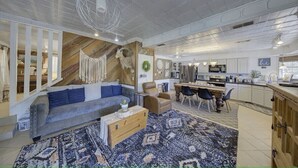 A spacious living area with a sofa, coffee table, and a dining table with chairs. A kitchen is visible in the background. - Paradise Canyon (Ingram)