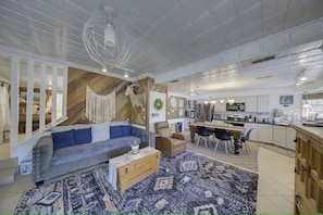 A spacious living area with a sofa, coffee table, and a dining table with chairs. A kitchen is visible in the background.