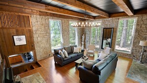 Amplia sala de estar con pared de piedra, vigas de madera en el techo, un sofá grande, una mesa de centro y una chimenea.