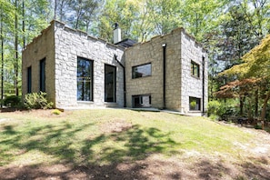 A modern stone house with large windows, a chimney, and a well-maintained lawn.