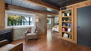 Una habitación con pared de piedra, vigas de madera en el techo, un ventanal grande, una estantería y una cama.
