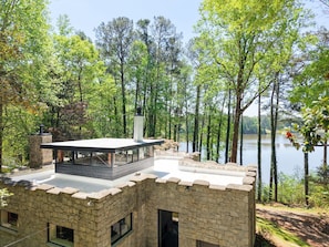 A stone building with a glass balcony overlooking a lake surrounded by trees.