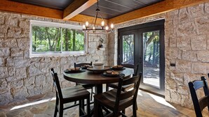 Una habitación con paredes de piedra, una mesa redonda y sillas, una araña y vistas a árboles a través de amplios ventanales.