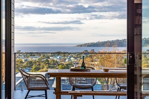 A balcony with a table and chairs, overlooking a coastal town and the sea. - Spacious Bay View Home for Groups (Dromana)