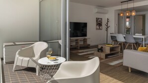 Ein modernes Wohnzimmer mit Glastür zum Balkon, einem Flachbildfernseher und einem Essbereich mit Stühlen und Tisch.