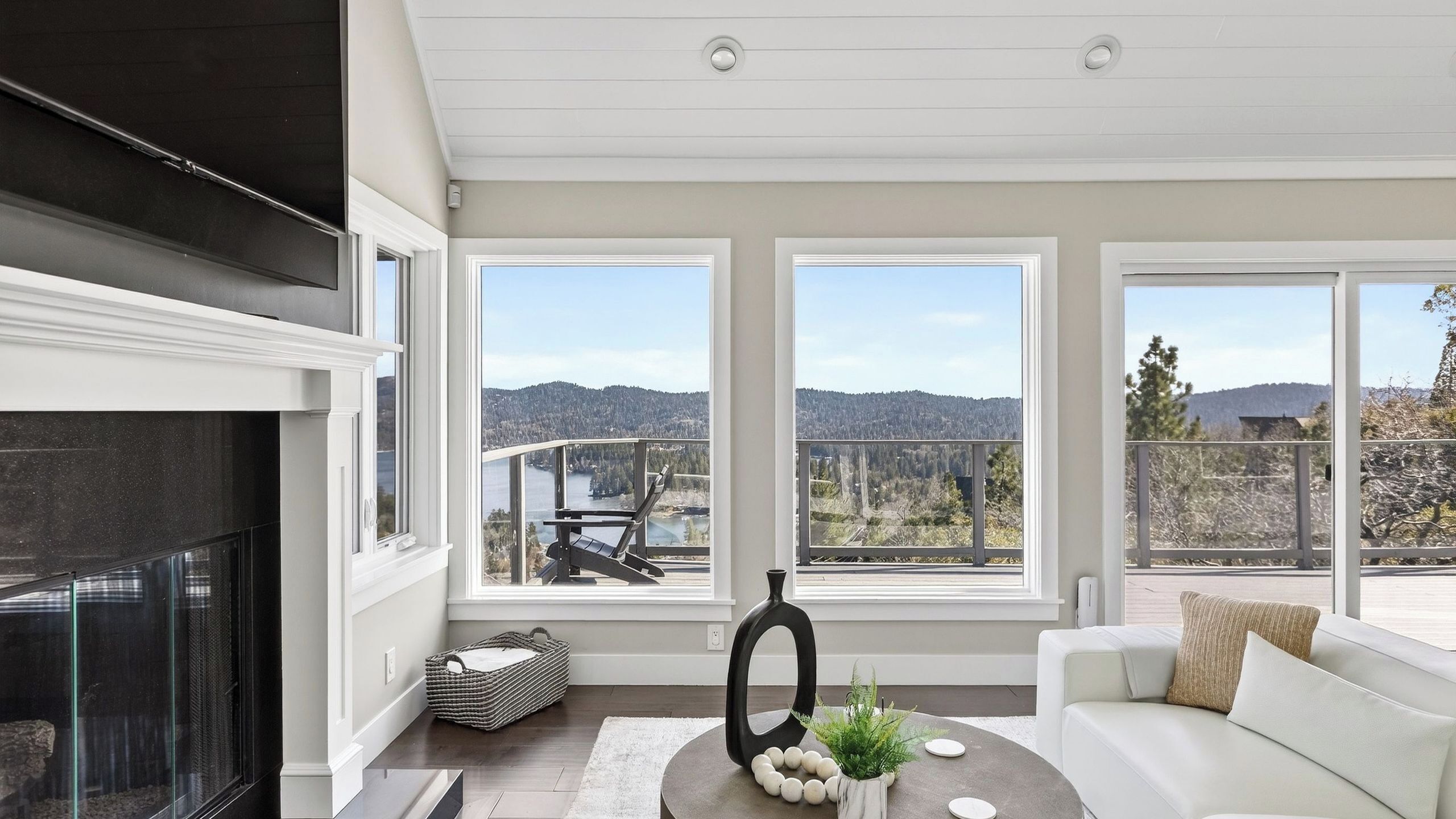 A modern living room with a fireplace, large windows offering a scenic view of mountains and a lake, and a cozy seating area.