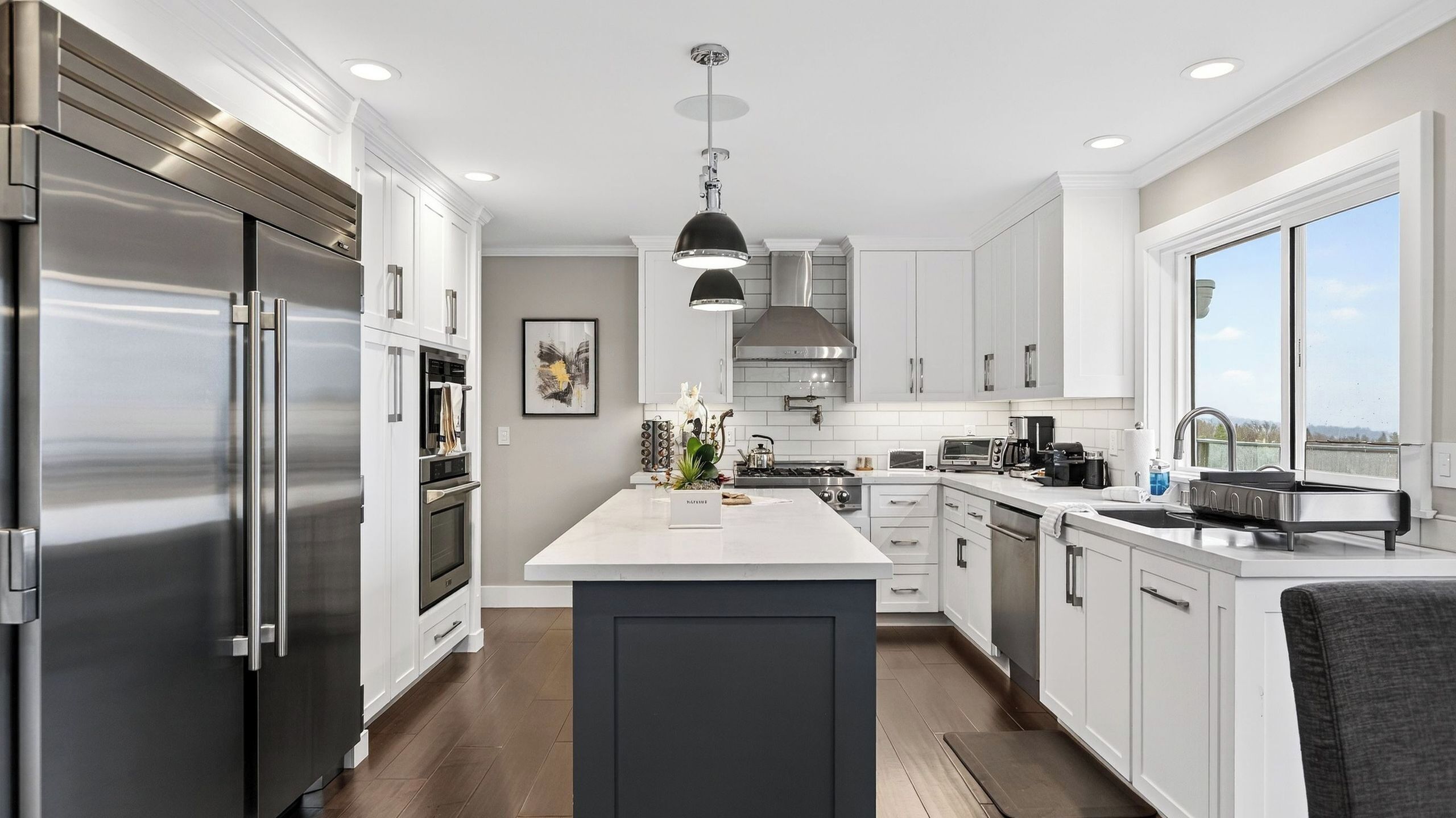 A modern kitchen with stainless steel appliances, a central island, and a large window providing a view.