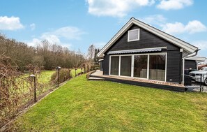 Ett svart hus med en stor skjutdörr i glas, en träveranda och en gräsklädd trädgård.