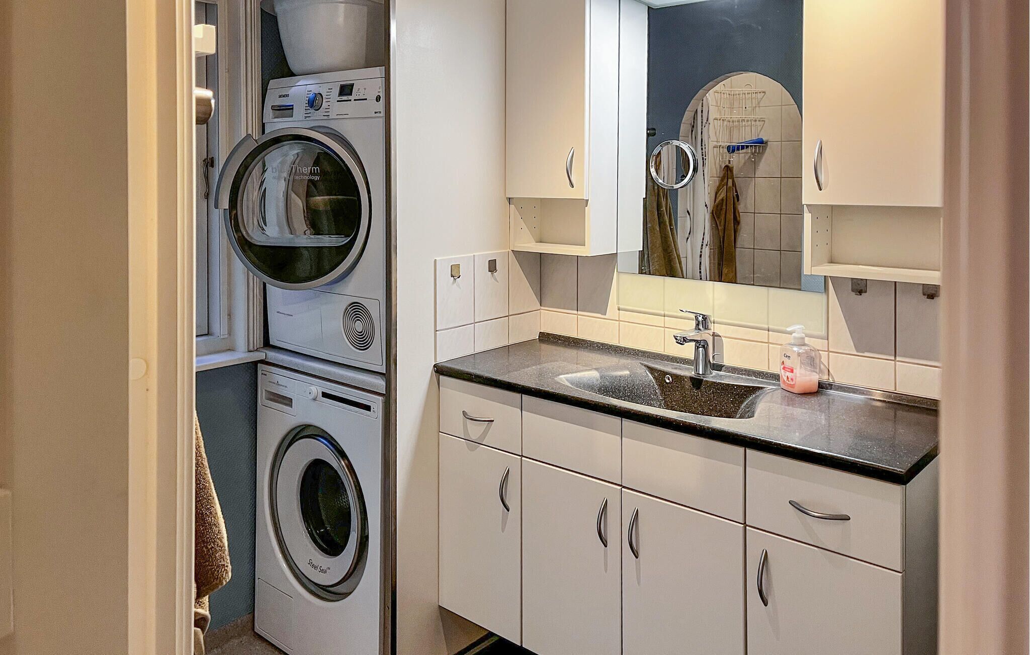 Une petite buanderie équipée d’un lave-linge, d’un sèche-linge et d’un évier surmonté d’un miroir.