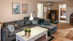 Een gezellige woonkamer met een grijze bank, een witte salontafel met potplanten, een open haard en een bed op de achtergrond.