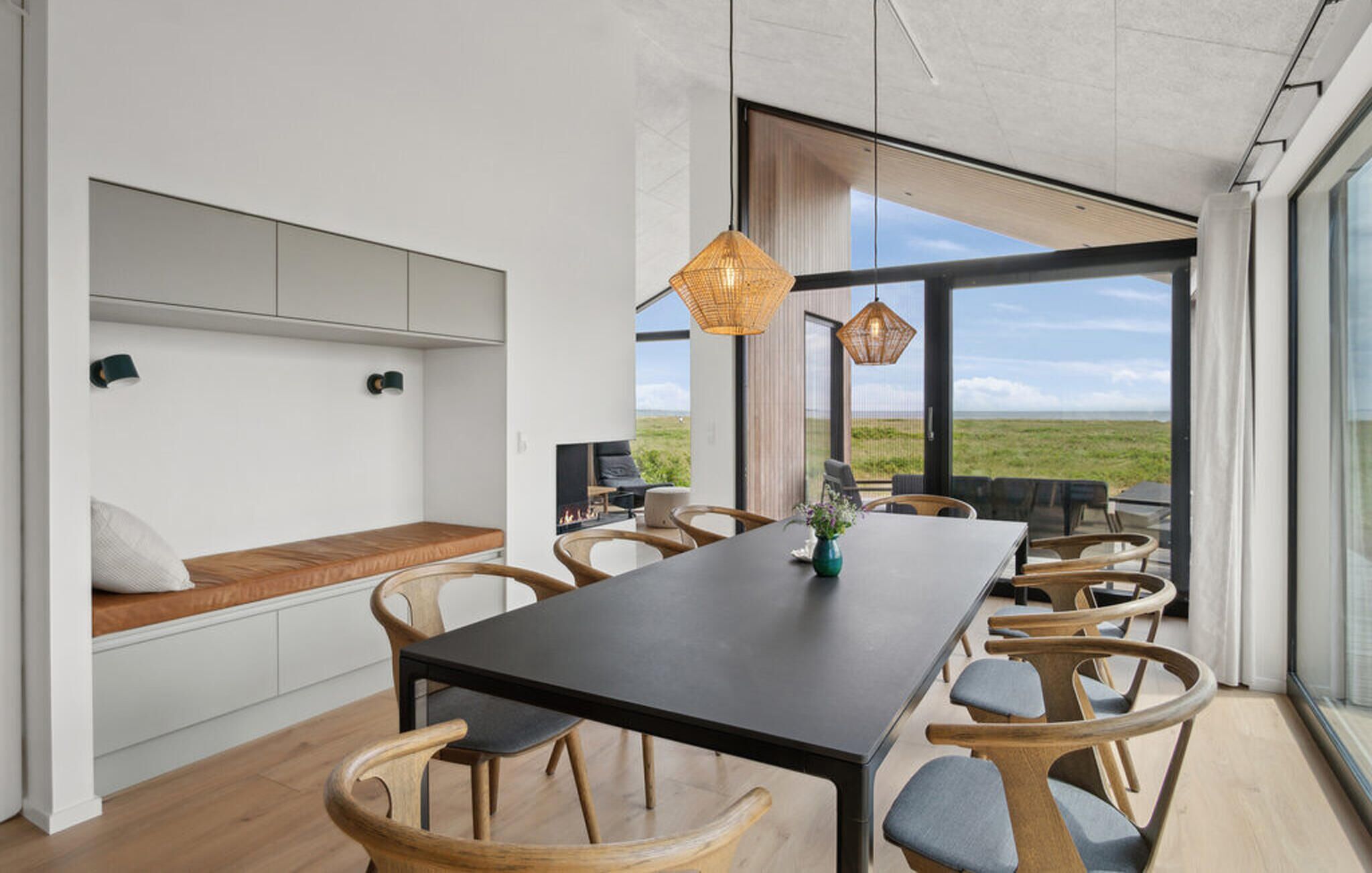 Ein moderner Essbereich mit einem langen Tisch, Holzsesseln und Blick auf die Landschaft durch große Fenster.