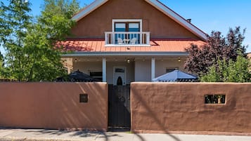 Une maison à deux étages avec un balcon, une porte d’entrée et une entrée fermée par un portail.