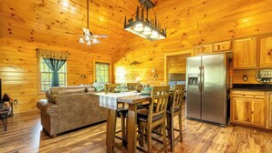 A wooden cabin interior with a dining table, chairs, a sofa, a refrigerator, and a ceiling fan.