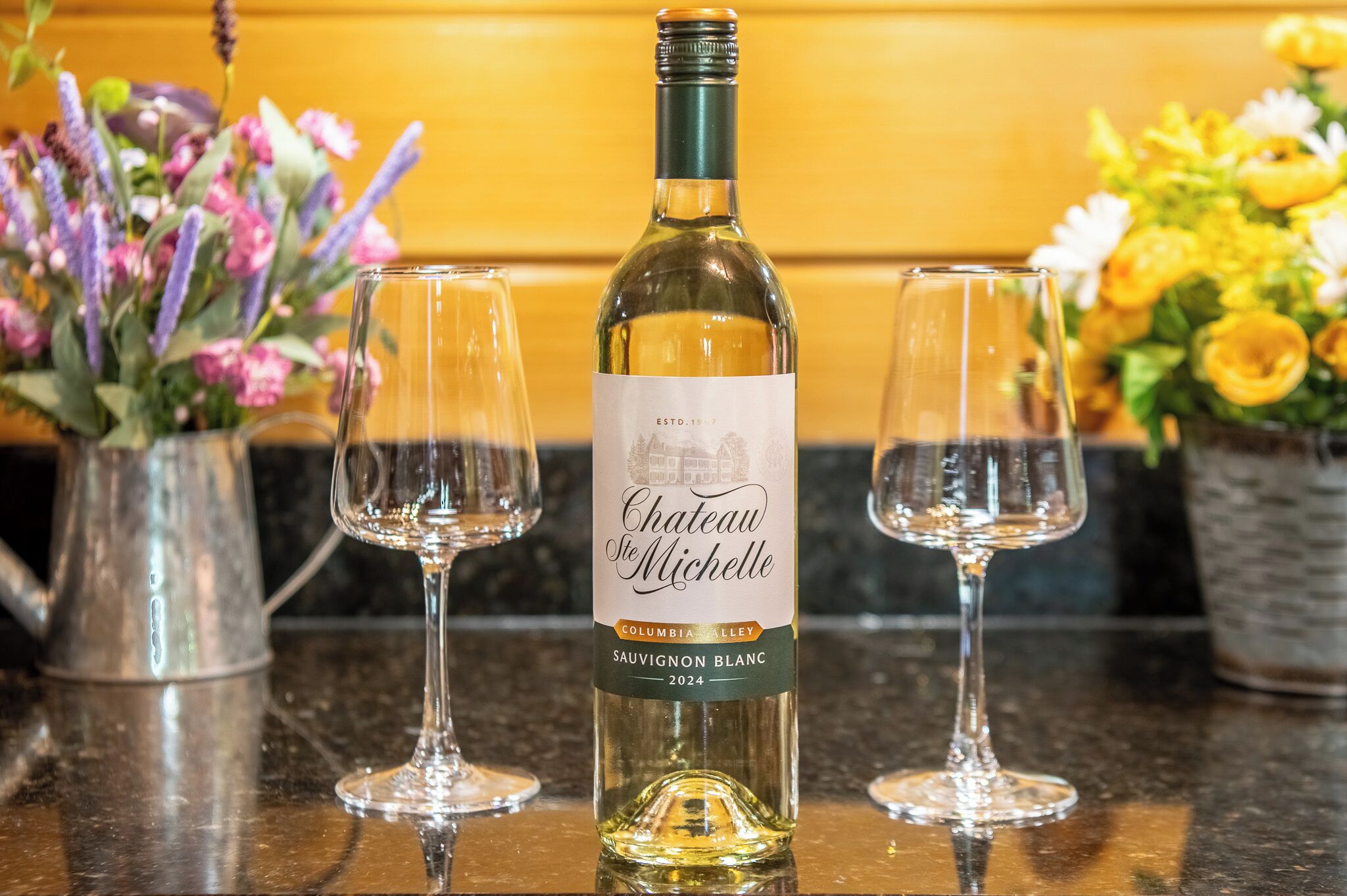 A bottle of Chateau Ste Michelle Sauvignon Blanc 2024 on a counter with two empty wine glasses.
